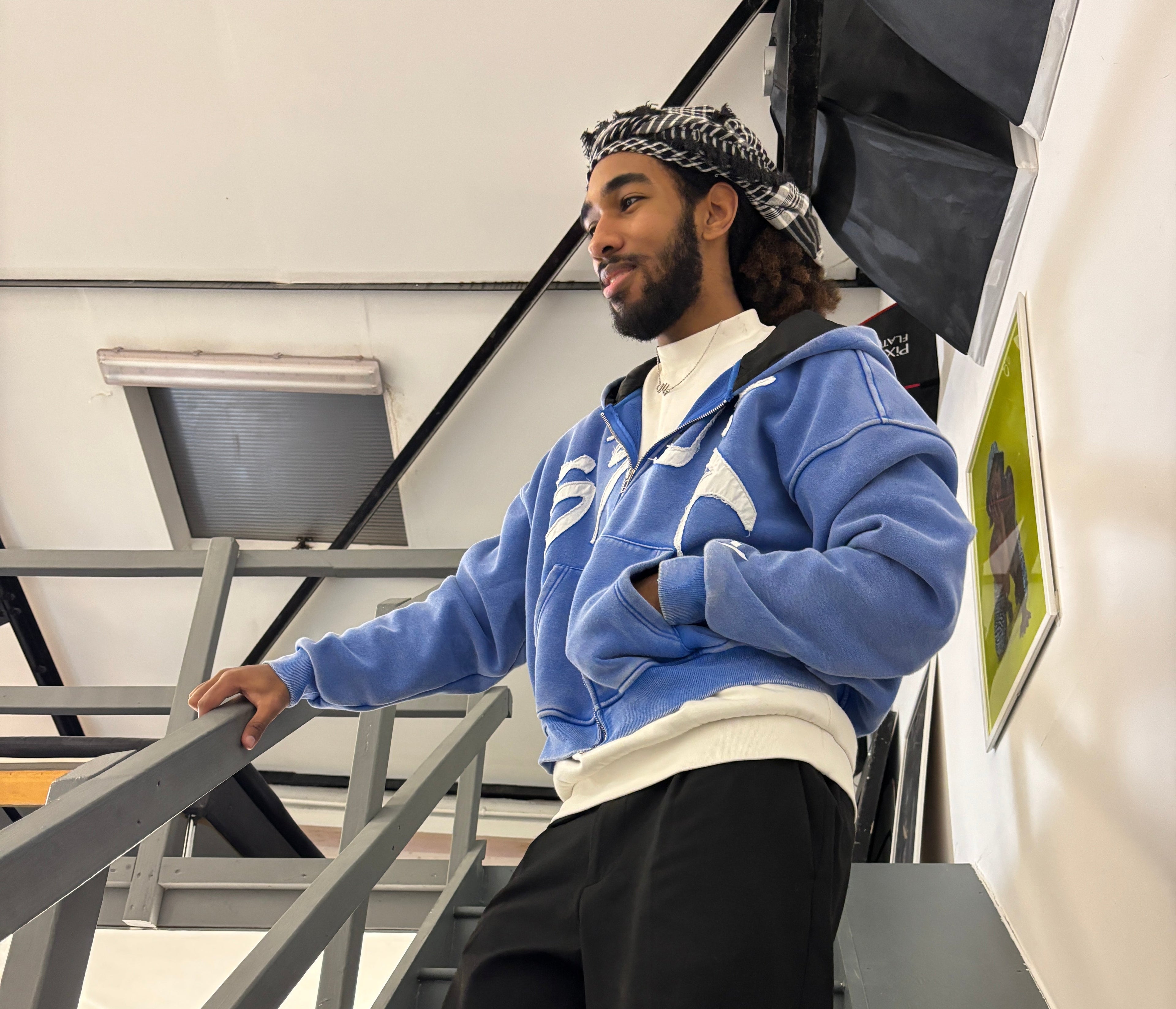 Person wearing a blue jacket and black pants sitting on a staircase.