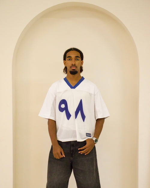 Person wearing a white jersey with blue number '91' standing in front of a beige archway.